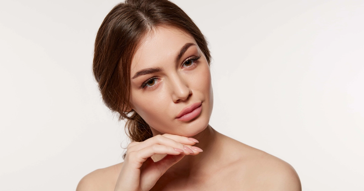 Studio portrait of a young woman with dark hair, clear skin, and a thoughtful expression, hand under chin, bare shoulders, on a plain bright background for Matrix IR in New York, NY.